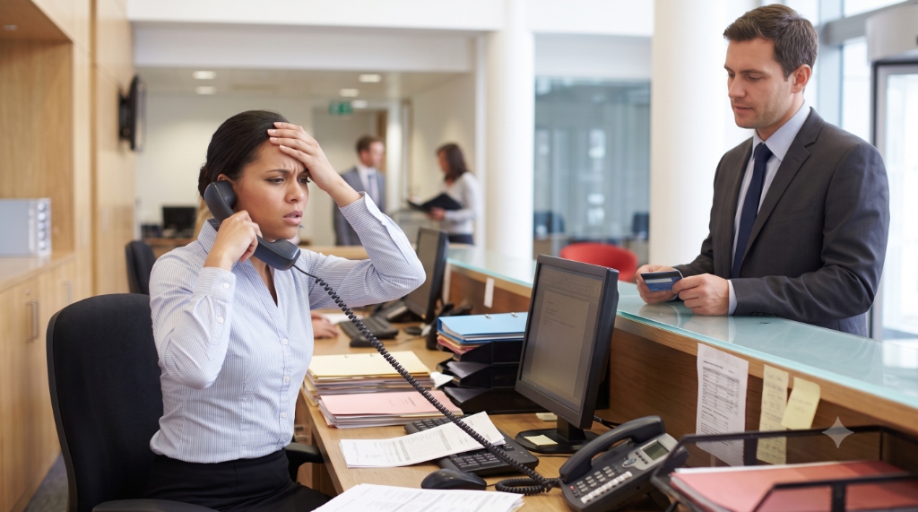 Overwhelmed receptionist trying to take an inbound call while helping an in-person client